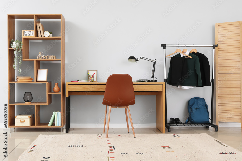 Interior of stylish room with modern workplace and school uniform on rack