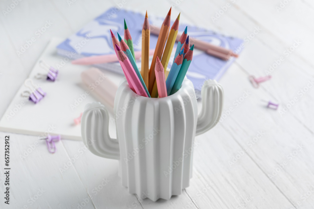 Stylish holder with color pencils, notebooks and paper clips on light wooden background