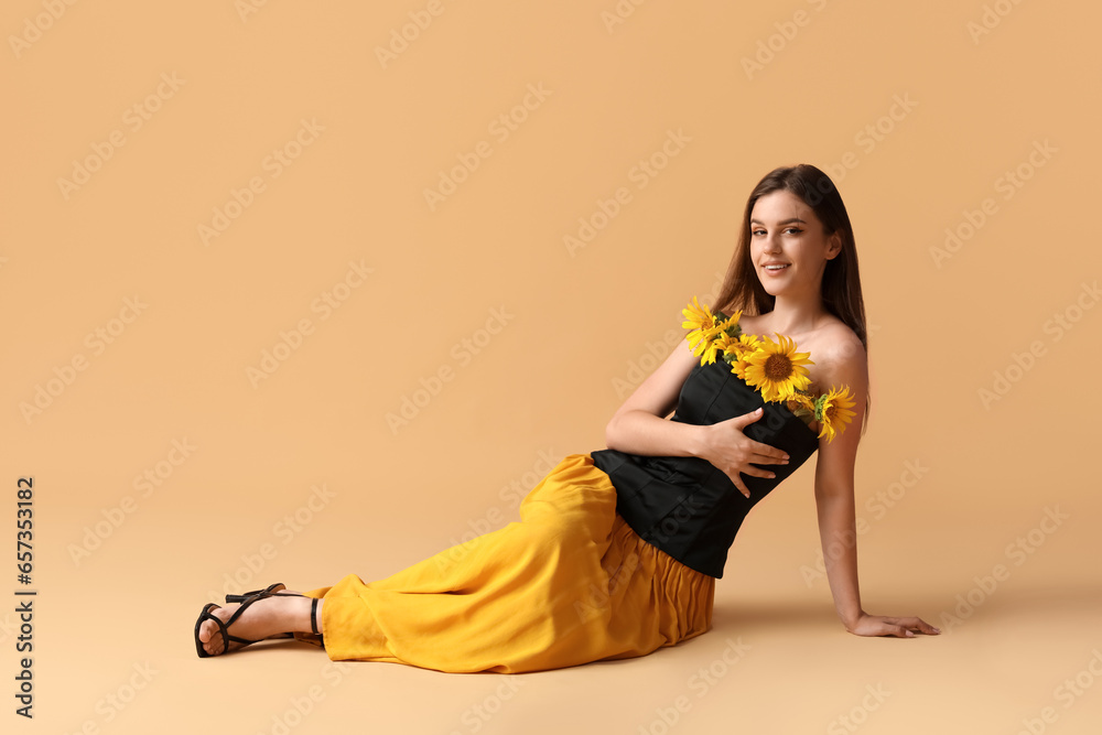 Happy young woman with beautiful sunflowers sitting on orange background