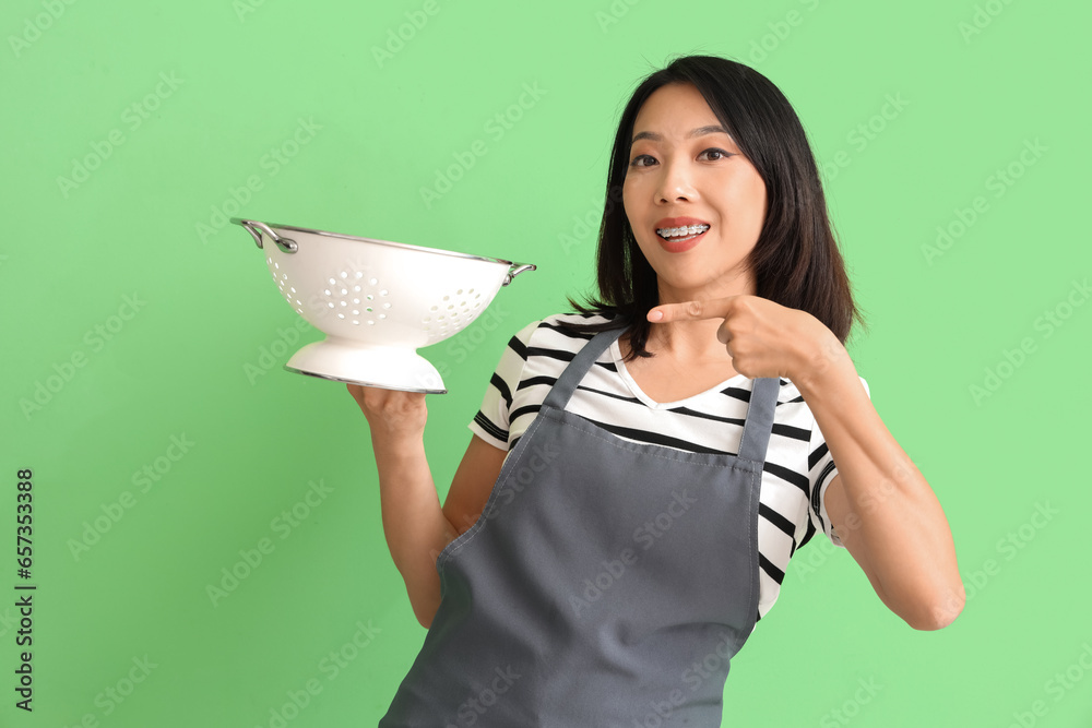 Happy beautiful Asian woman pointing at colander on green background