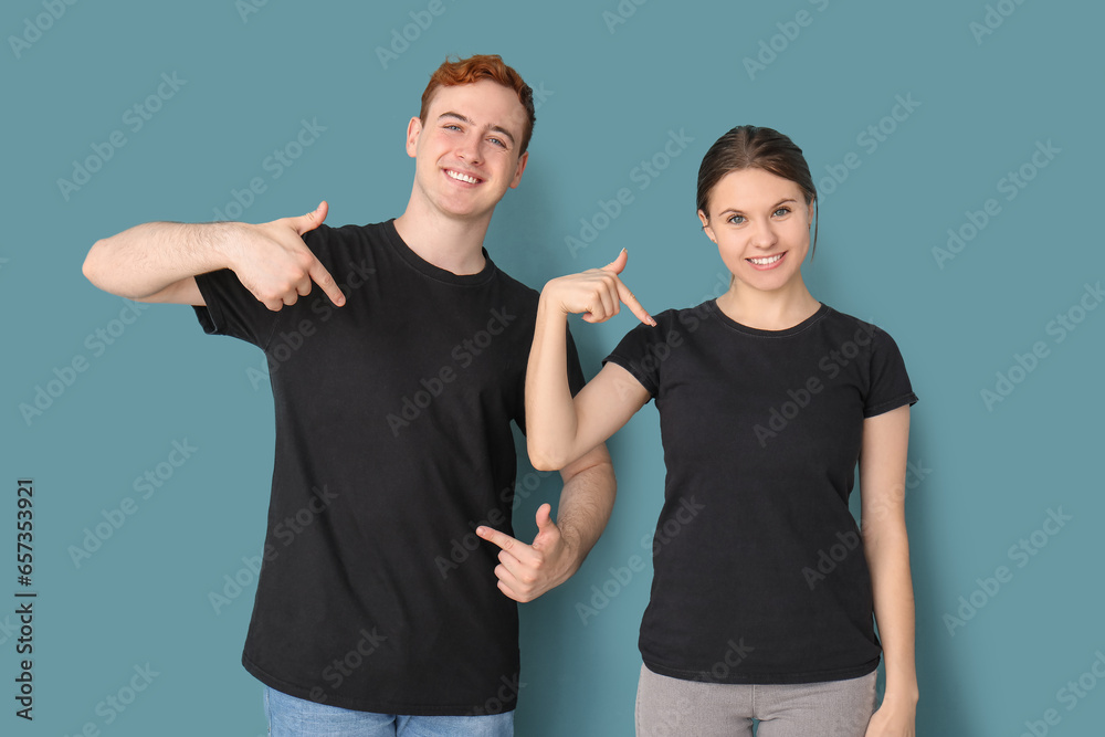 Young couple pointing at their black t-shirts on blue background