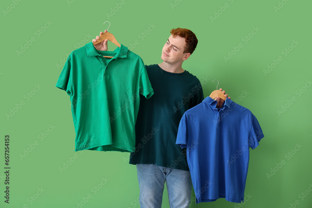 Young man choosing t-shirt on green background