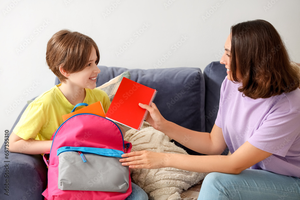 Mother helping her little son to pack schoolbag in living room