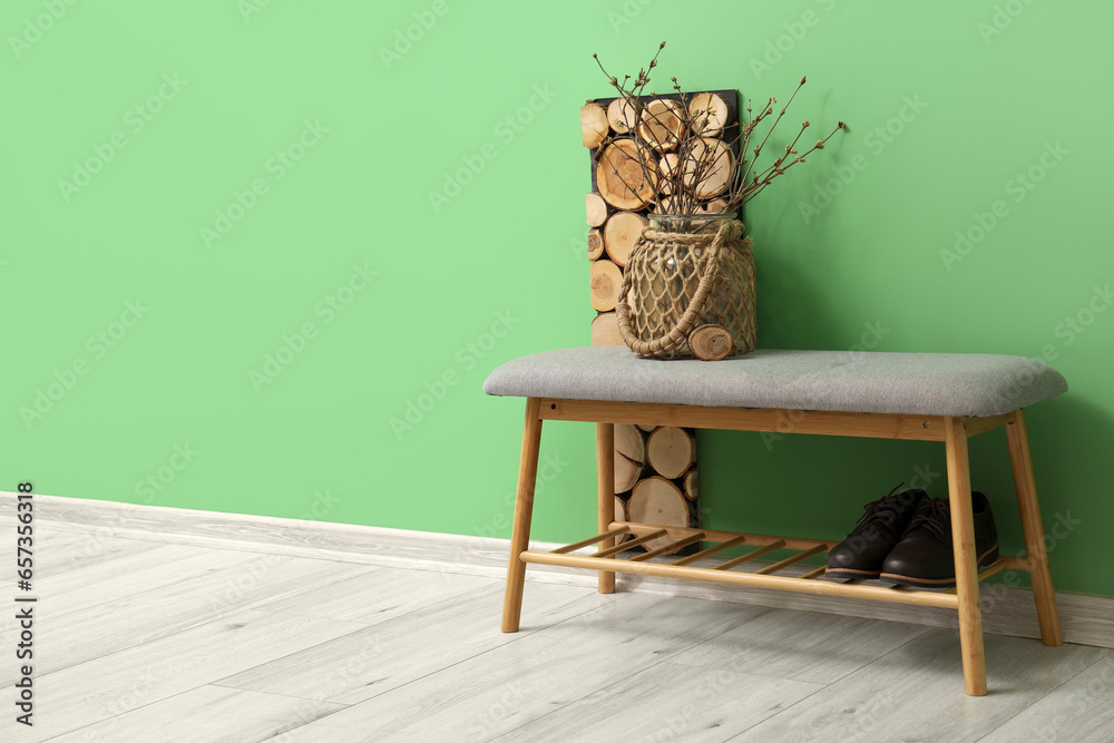 Soft bench with vase and shoes near green wall in room