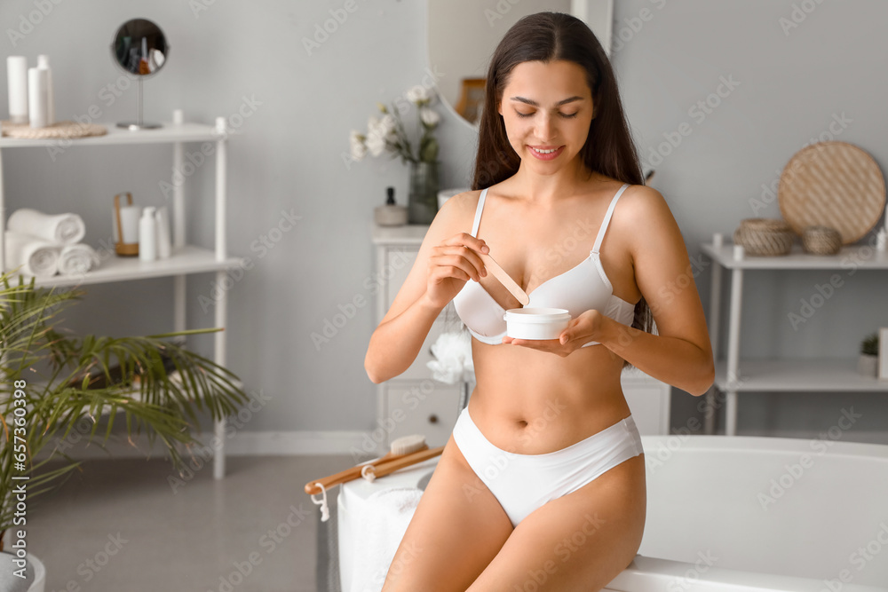 Beautiful young woman with sugaring paste and wooden stick in bathroom