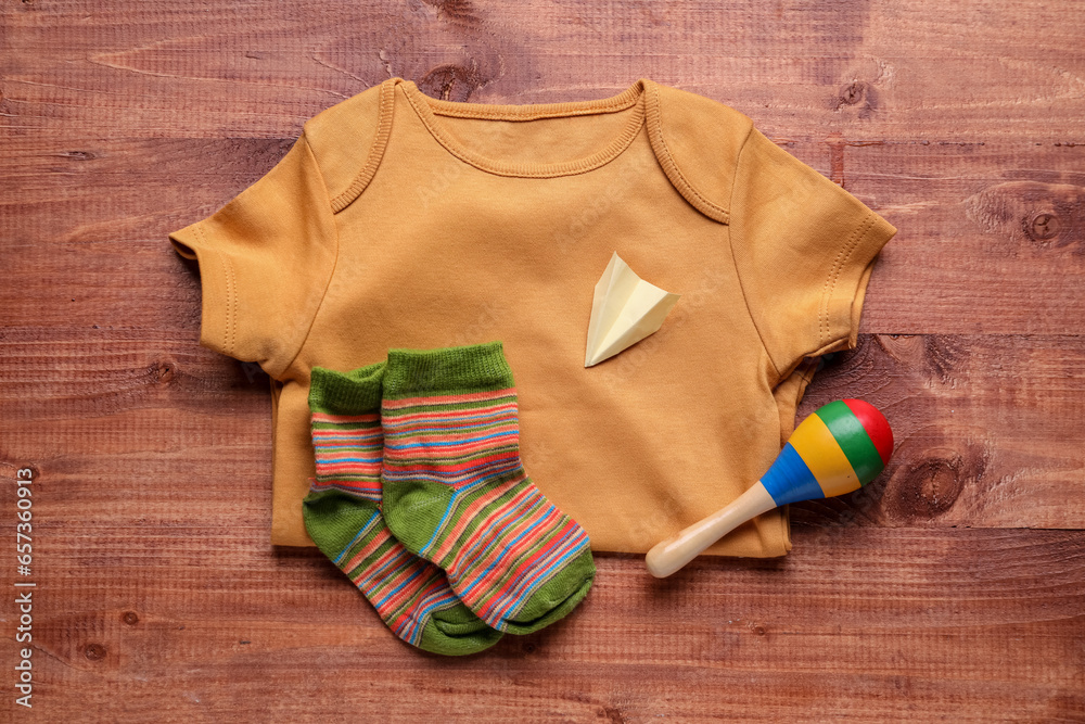 Baby bodysuit, socks and rattle on wooden background