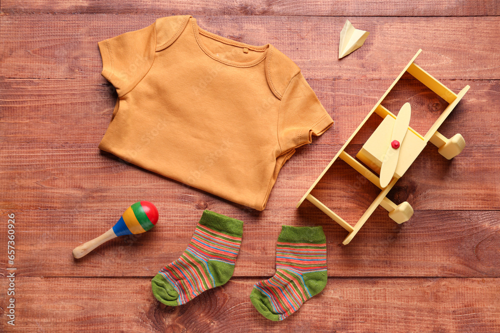 Baby bodysuit, socks and toys on wooden background