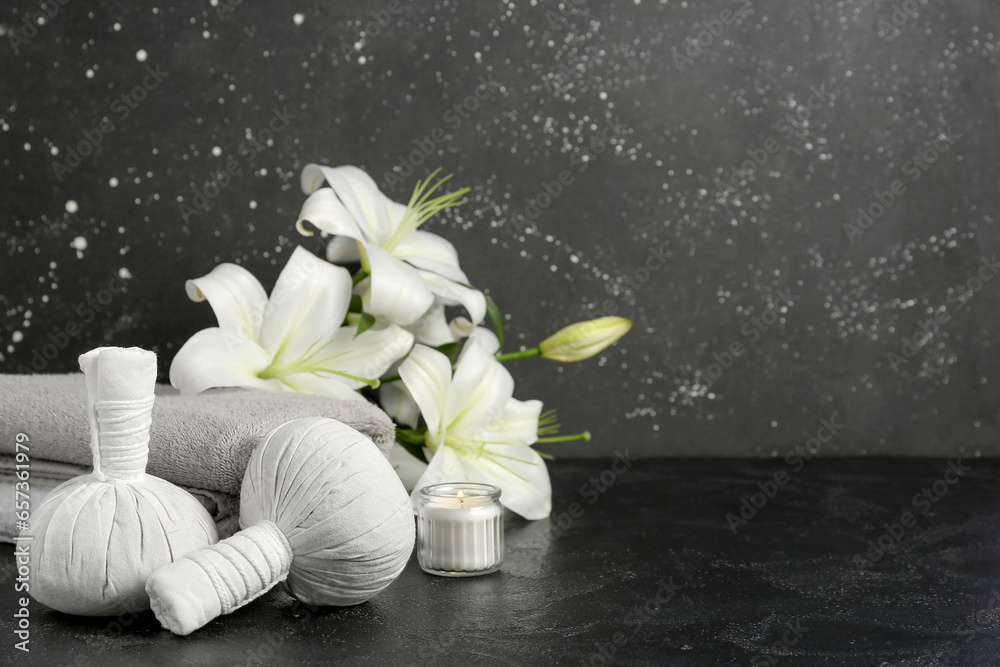 Massage herbal bags, clean towels and beautiful lily flowers on dark background