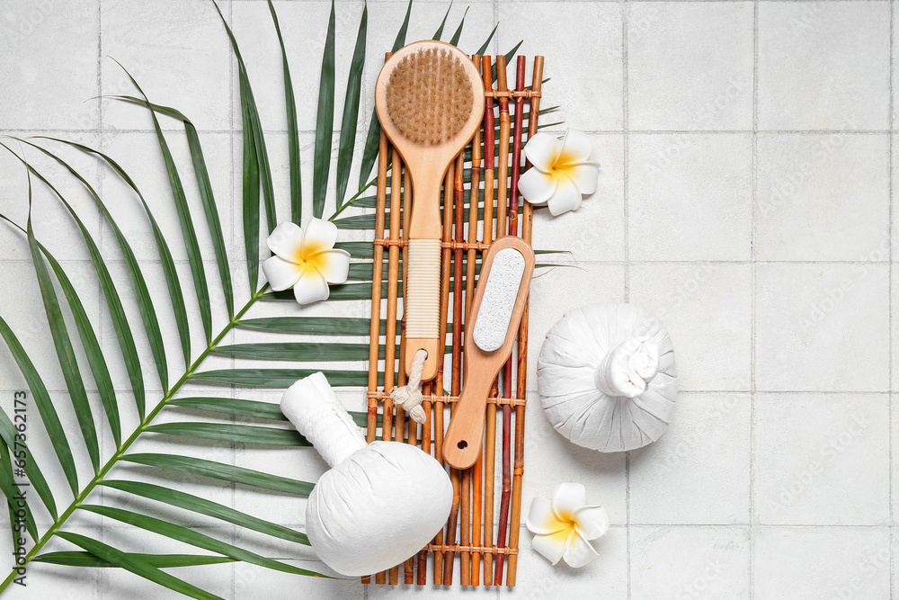 Composition with spa accessories, palm leaf and tropical flowers on light tile background