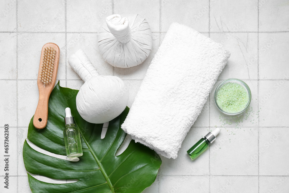 Composition with spa accessories, bottles of essential oil and palm leaf on light tile background