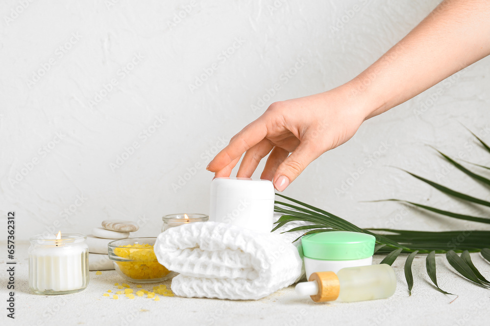 Female hand with cosmetics, spa accessories and palm leaf on light background