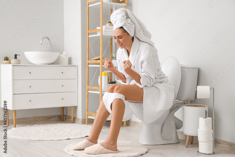 Young woman sitting on toilet bowl in restroom