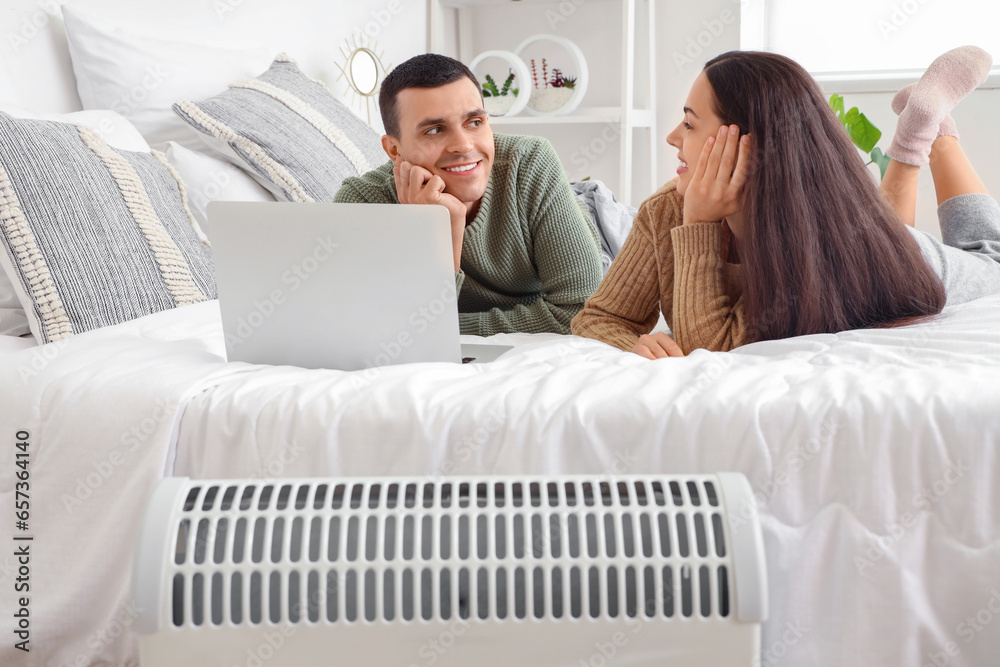 Young couple with laptop warming near radiator in bedroom