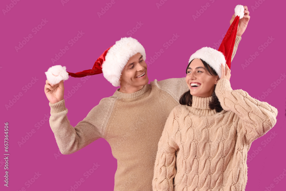 Happy young couple in Santa hats on purple background