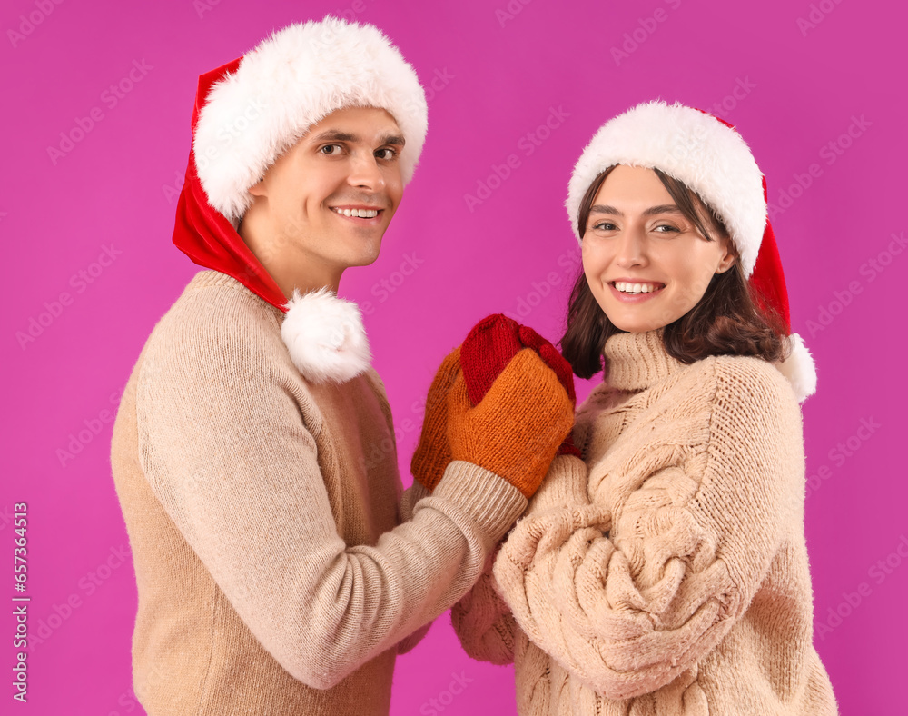 Happy young couple in Santa hats and warm gloves on purple background