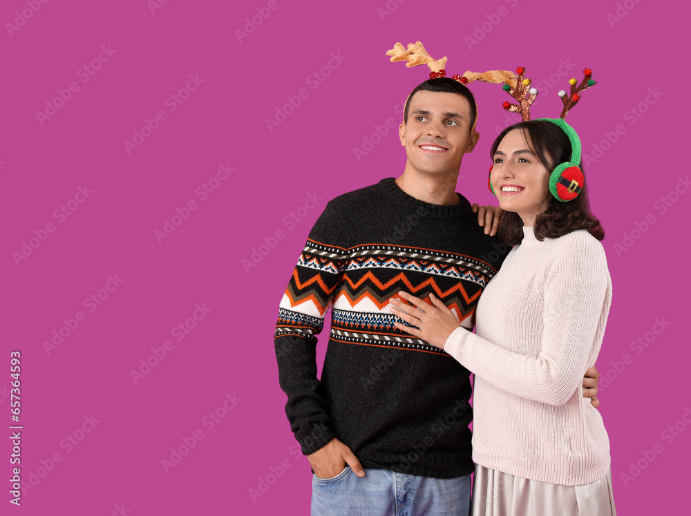 Happy young couple in Christmas reindeer horns on purple background