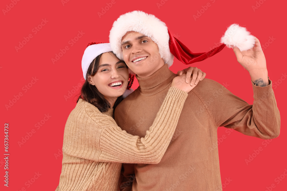 Happy young couple in Santa hats hugging on red background