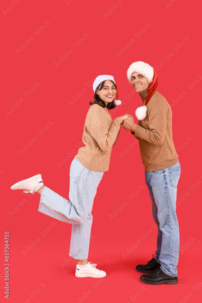 Happy young couple in Santa hats on red background