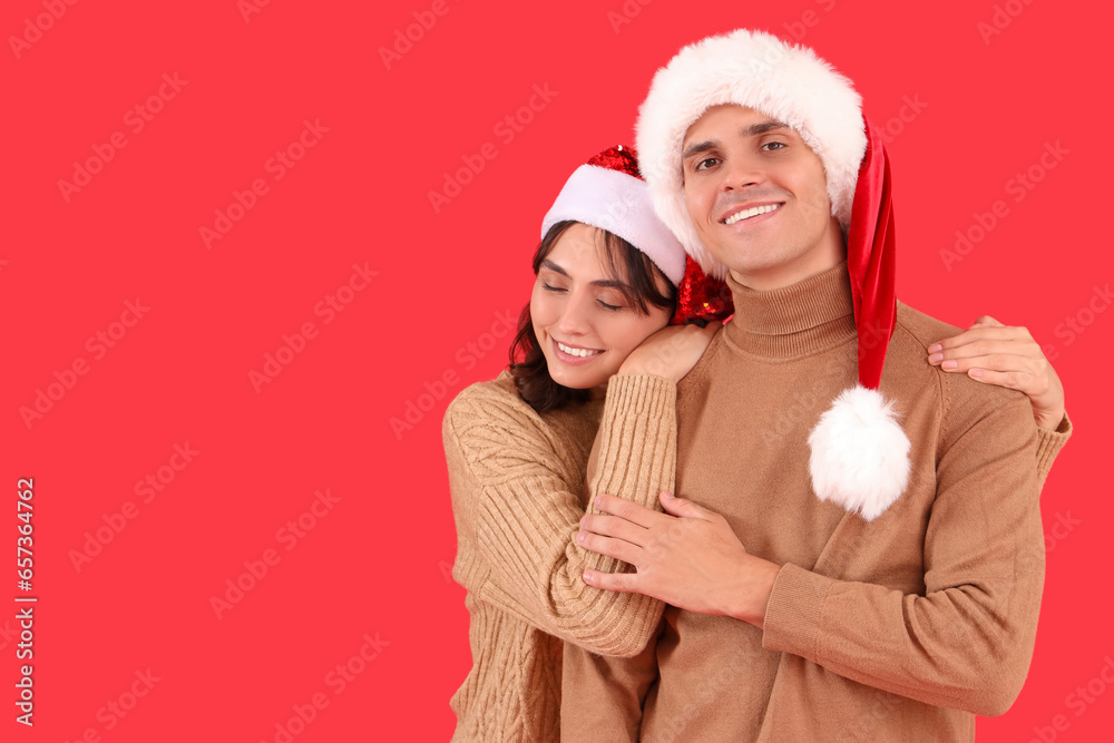 Happy young couple in Santa hats hugging on red background