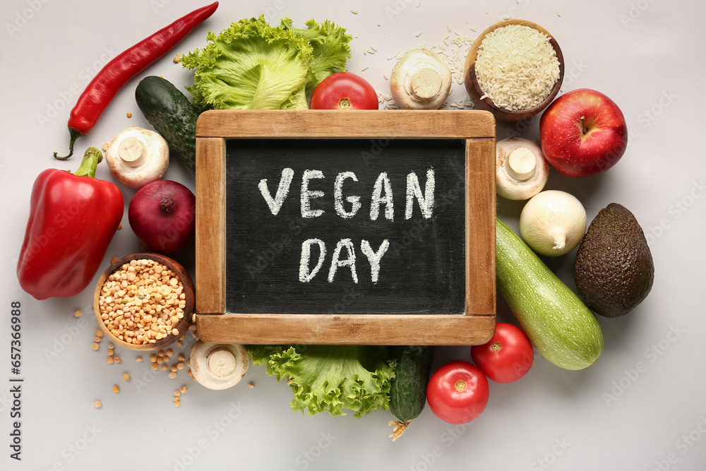 Board with text VEGAN DAY and different healthy products on grey background