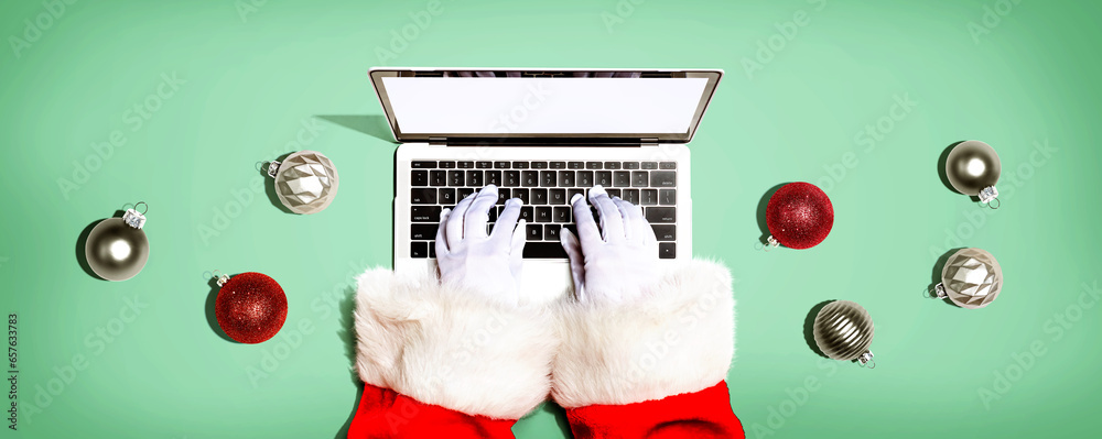 Santa Claus using a laptop computer with Christmas baubles from above