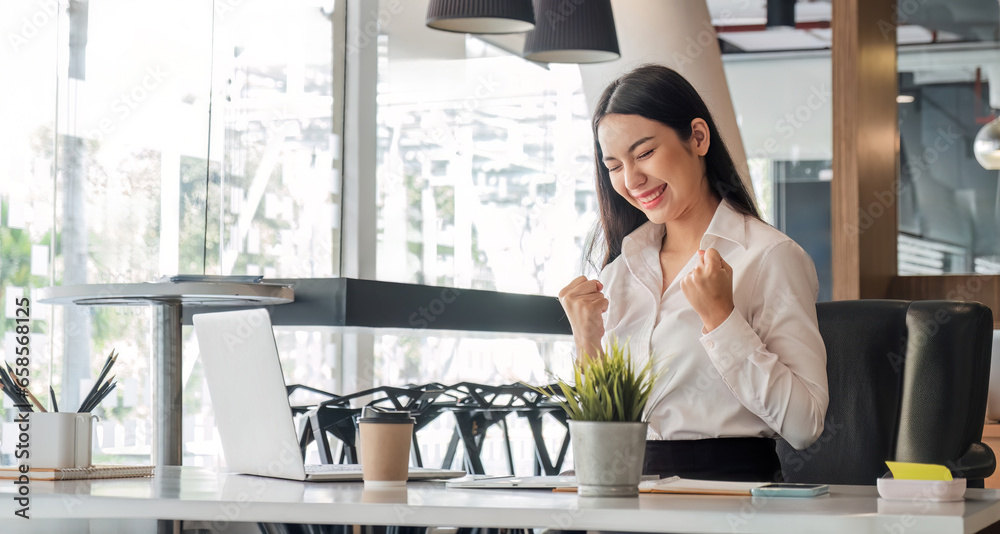 happy Asian businesswoman are delighted to raise hands in success using a laptop at the office.