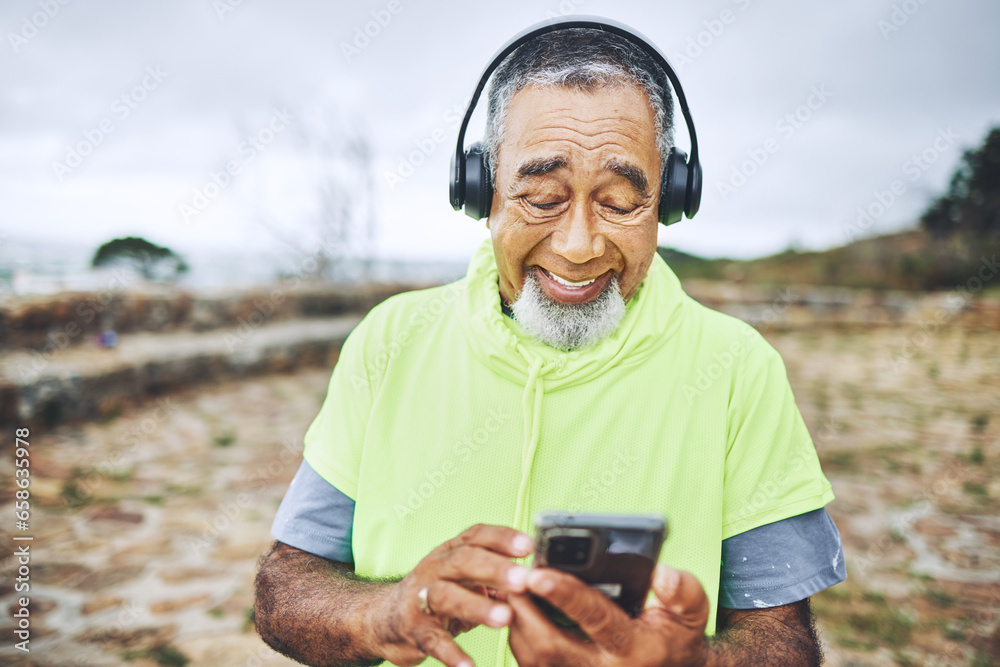 Phone, headphones and senior man hiking for health, wellness or cardio training on a mountain. Smile, cellphone and elderly male person scroll on the internet for music for outdoor trekking in woods.