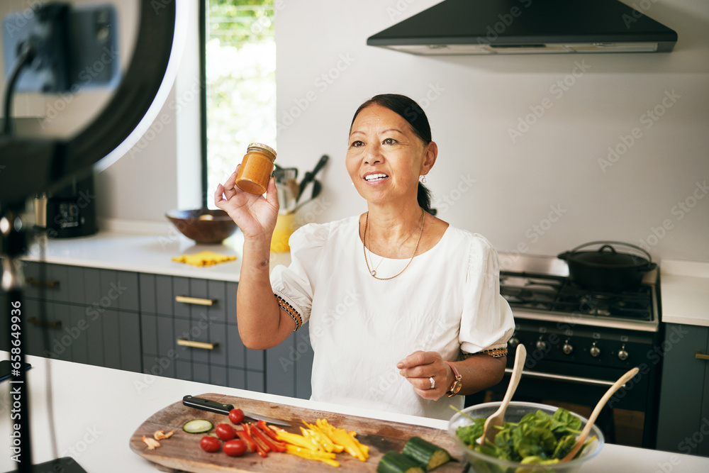 Asian woman, happy and live streaming for cooking with bottle, healthy food and social media blog in kitchen. Chef, mature influencer and vegetables for content creation, broadcast tutorial and phone