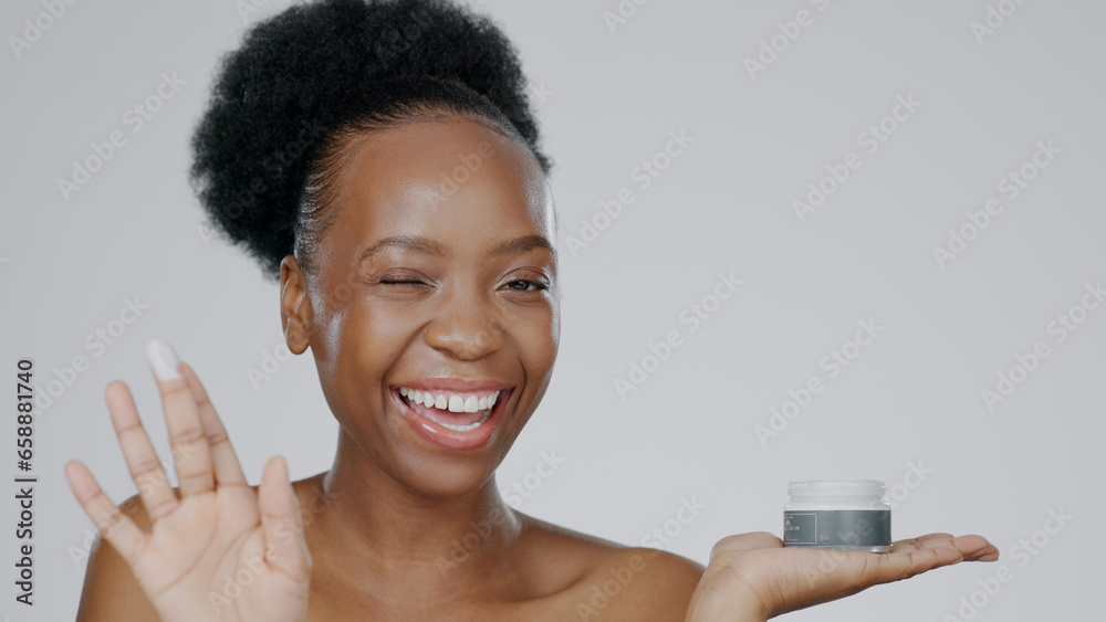 Woman, model and hand with cream for face, cosmetic and beauty aesthetic with wink for happiness. Black person, portrait and dermatology with smile for product, mockup and grey studio background