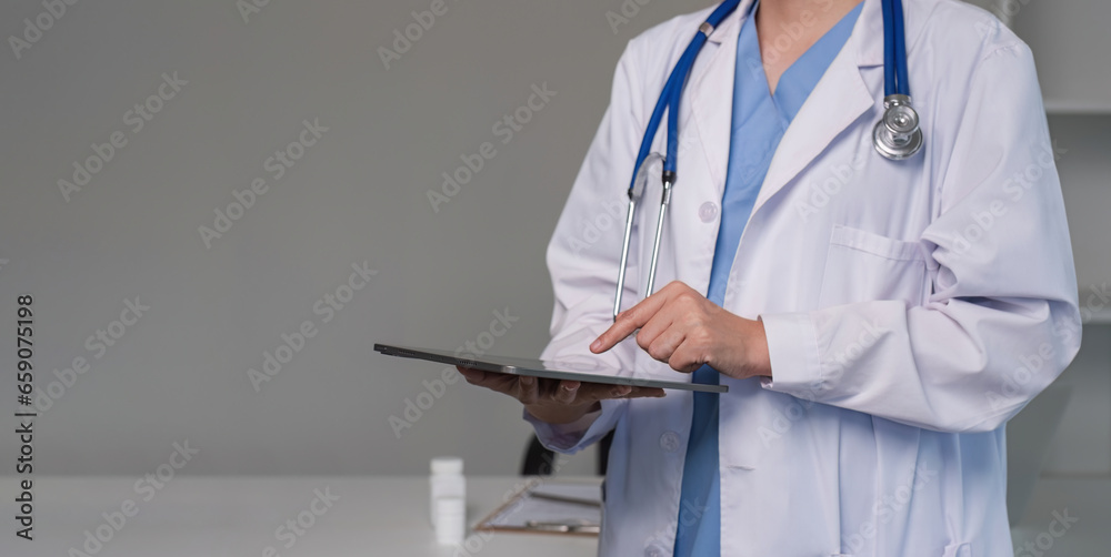 Close up female doctor holding a digital tablet wearing a medical coat and stethoscope in hospital