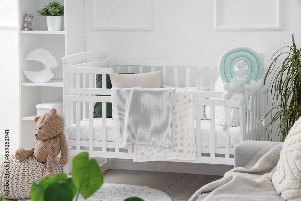 Stylish interior of childrens room in white tones with baby bed and shelving unit