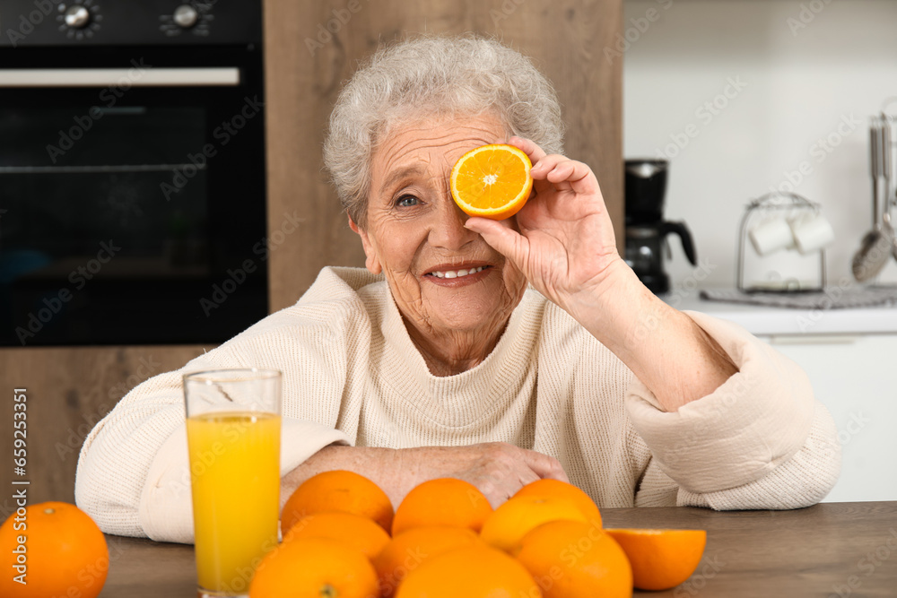 Senior woman with orange and glass of juice in kitchen