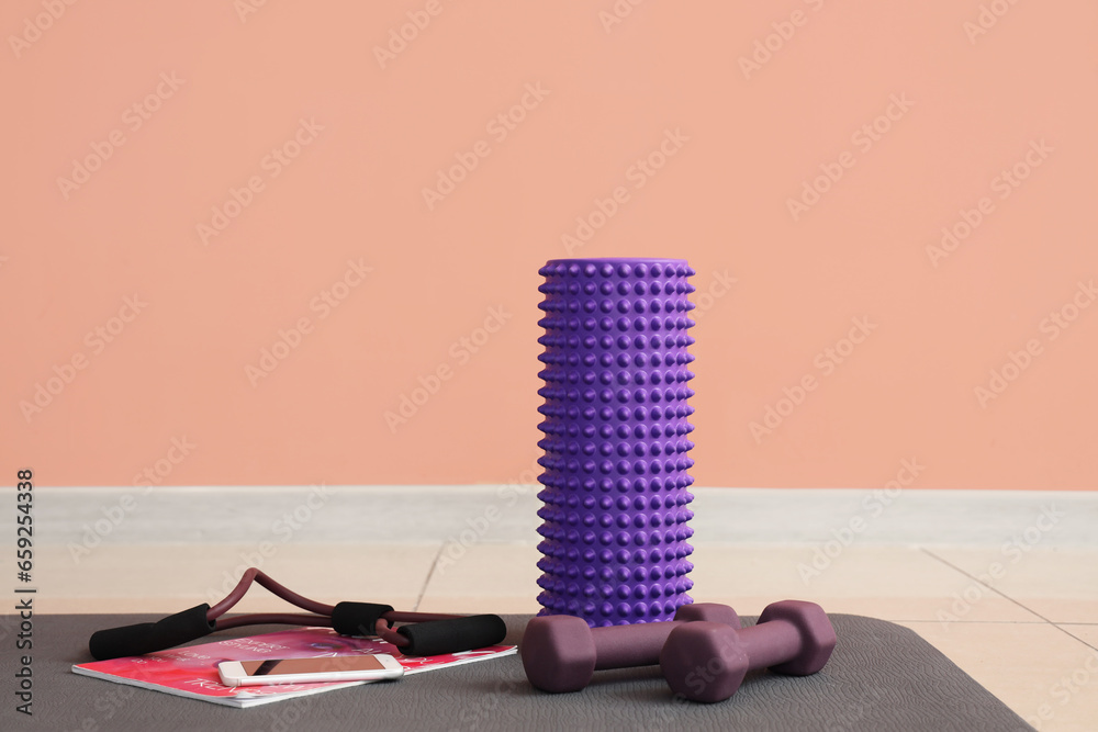 Sports equipment with mobile phone and magazine on fitness mat near pink wall in gym