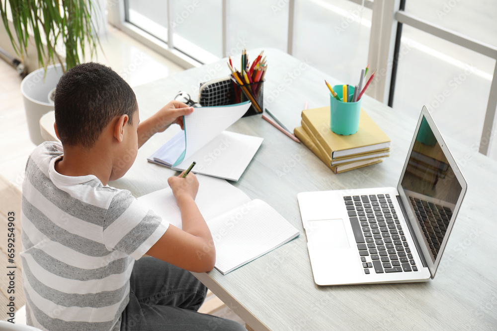 Little African-American boy studying online with laptop at home