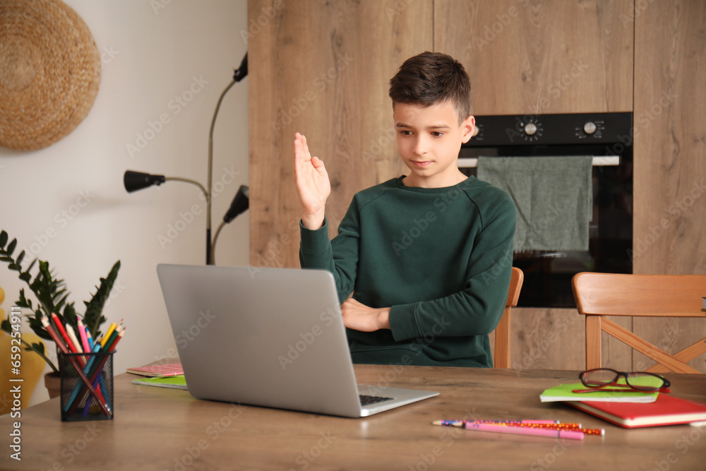 Little boy studying online with laptop in kitchen