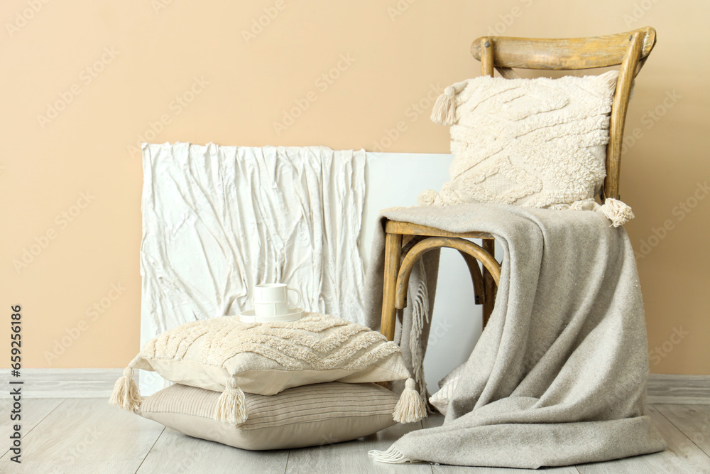 Armchair with cushions and blanket near beige wall