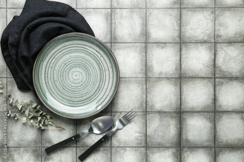 Clean plate with napkin and cutlery on grey tiled background