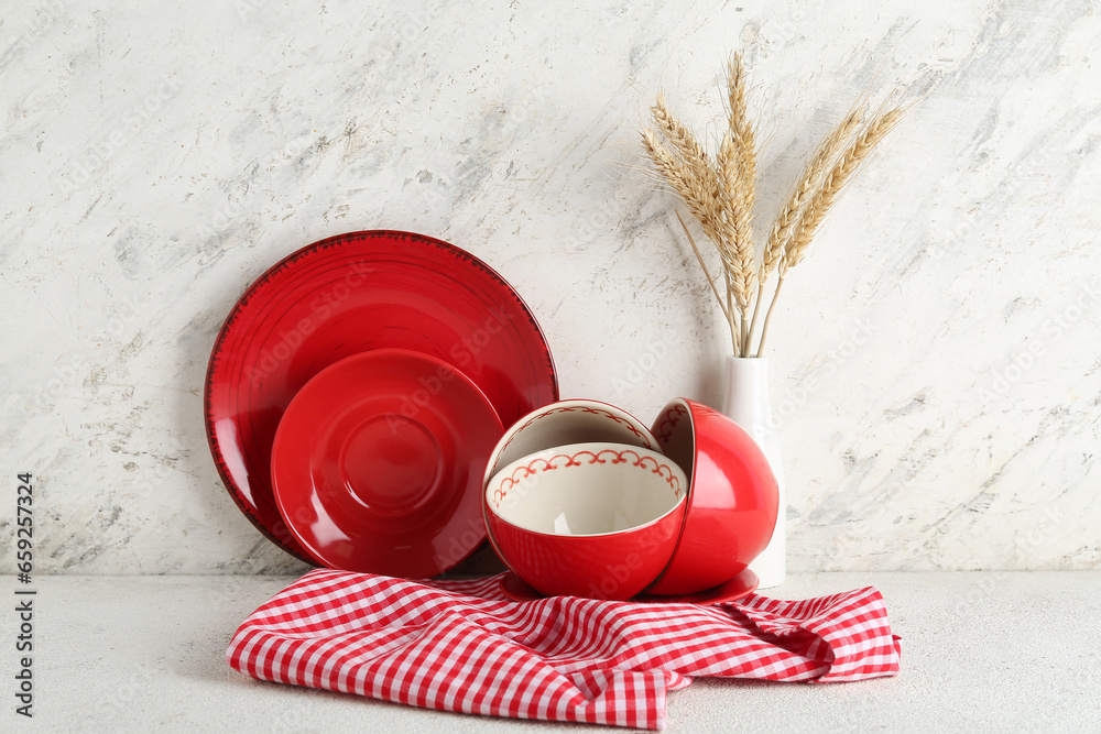 Red plates, bowls and vase with wheat spikelets on white table