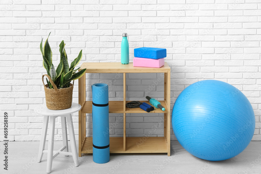 Wooden shelves with different fitness equipment near white brick wall