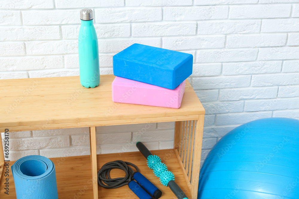 Wooden shelves with different fitness equipment near white brick wall