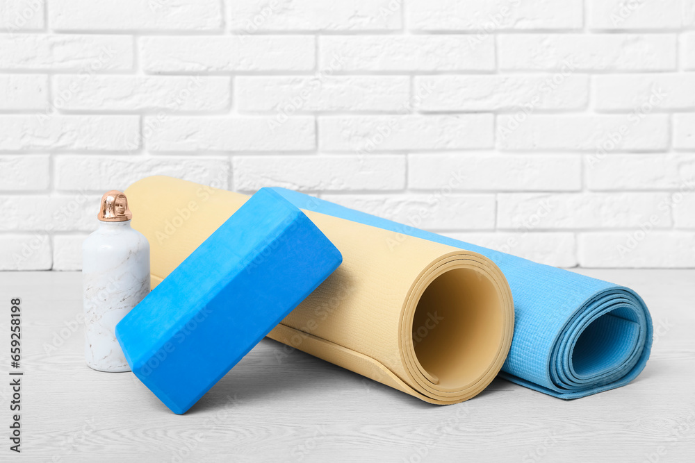 Yoga mats, foam exercise block and bottle of water on floor in gym, closeup