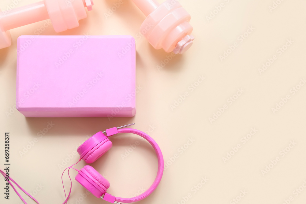 Yoga block, headphones and dumbbells on beige background