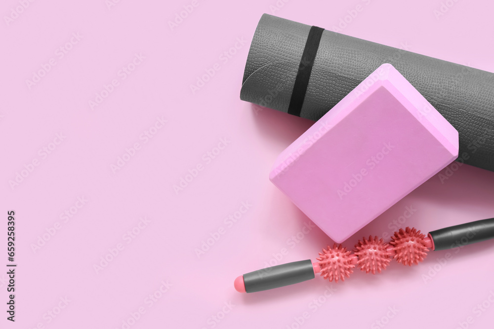 Yoga mat, foam exercise block and massage roller on pink background