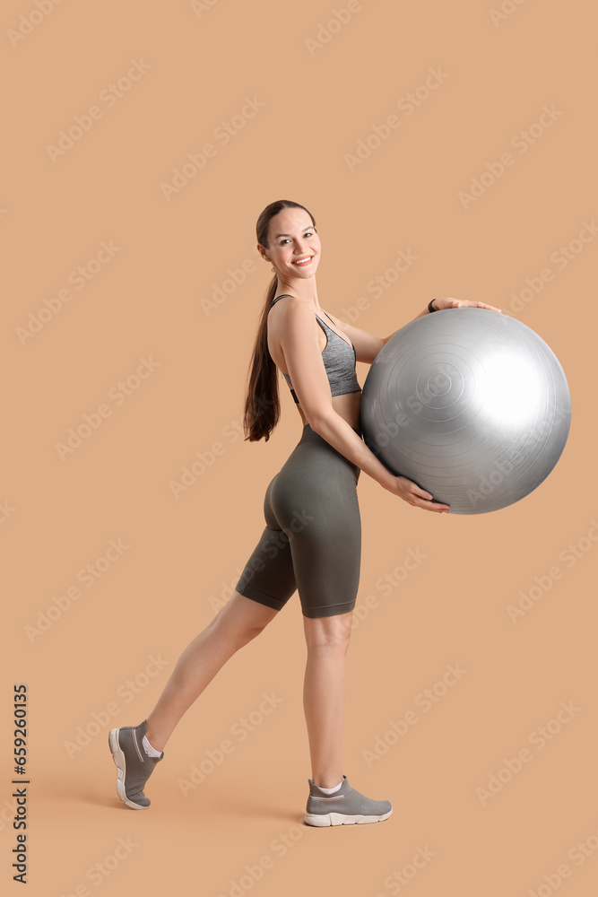 Sporty young woman with fitball on beige background