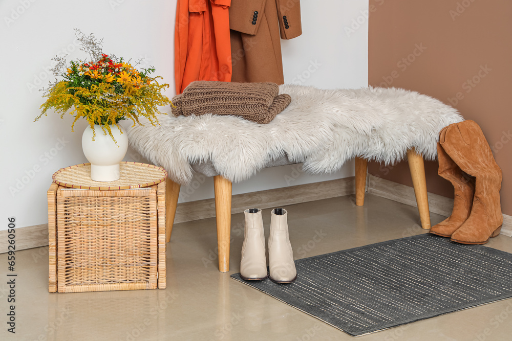 Vase with beautiful autumn flowers, bench and shoes in interior of modern hallway, closeup