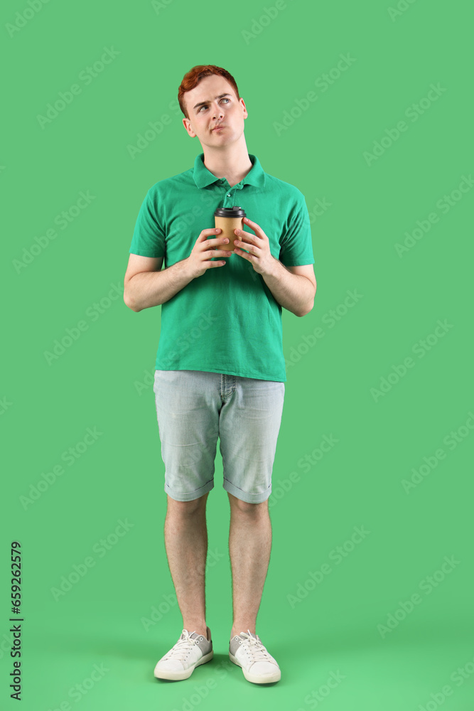 Thoughtful young redhead man with cup of coffee on green background