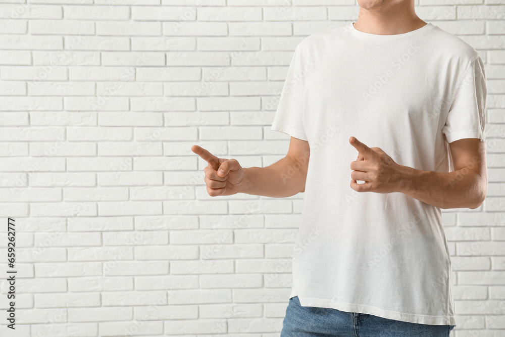 Man in stylish t-shirt pointing at something near white brick wall