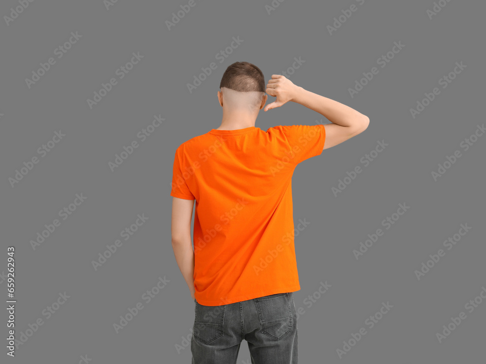 Man pointing at his stylish orange t-shirt on grey background, back view