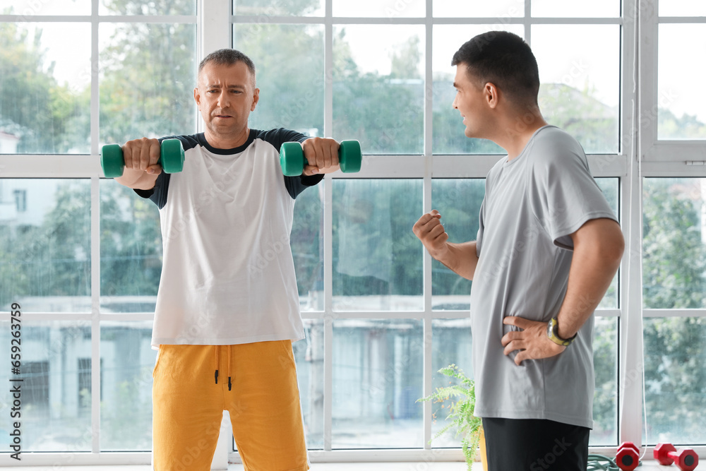 Mature man training with dumbbells and therapist in rehabilitation center