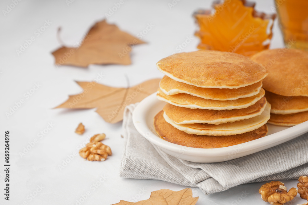 Plate of tasty pancakes with nuts and maple syrup on white background